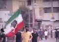 Manifestantes iraníes marchan por una calle urbana mientras uno de ellos sostiene una bandera de Irán en medio de protestas contra el régimen